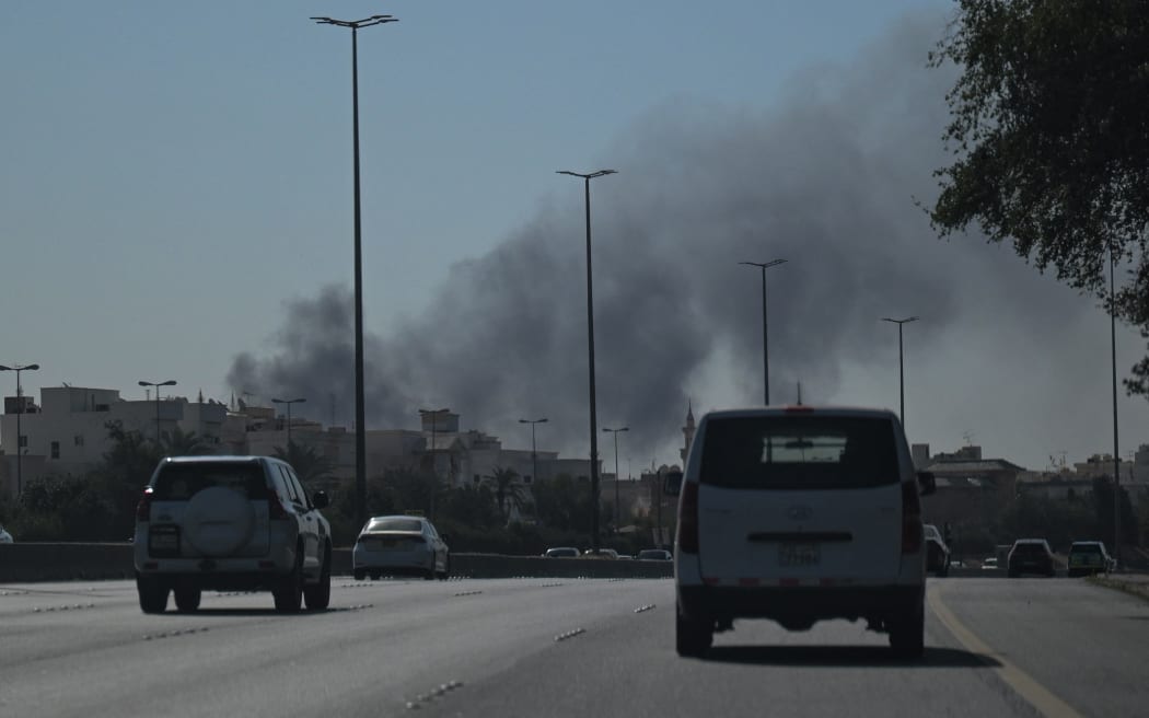 Motorists drive along a street as smoke rises from a reported Iranian strike in the area where the US Embassy is located in Kuwait City on March 2, 2026. Black smoke was seen rising from the US embassy in Kuwait City on March 2 after the latest volley of Iranian strikes, an AFP correspondent saw. (Photo by AFP)