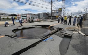 Workers stand by a partially collapsed road following an earthquake in Takatsuki, north of Osaka prefecture on 18 June, 2018.
