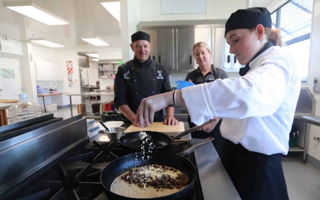 NorthTec Level 4 cookery student Astyn Hobman-Williams prepares a wallaby quesadilla for the Northland Field Days wild food giveaway under the watchful eyes of tutor chef Hughie Blues, left, and NRC Biosecurity Officer - Incursions Alicia King (until recently a NorthTec tutor in Environmental Management), 2025.