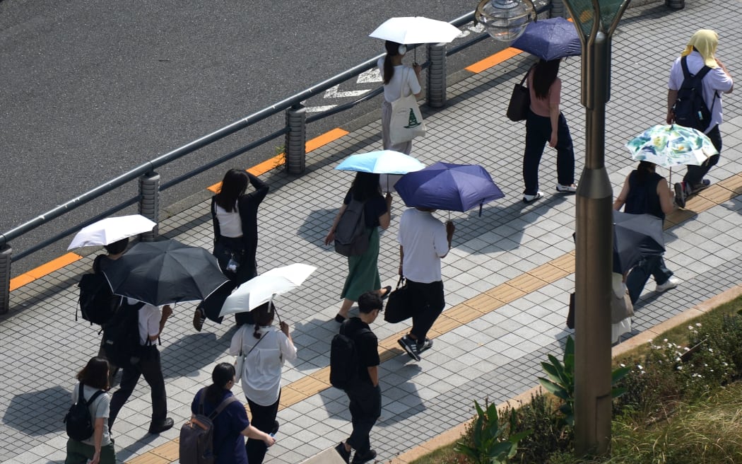 People with umbrellas walk in the scorching sun in Tokyo on September 1, 2025.