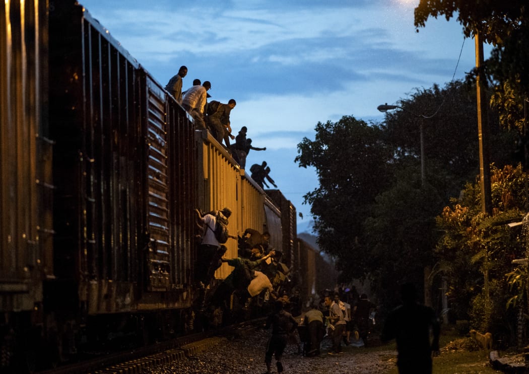 Undocumented migrants climb on a train known as "La Bestia".