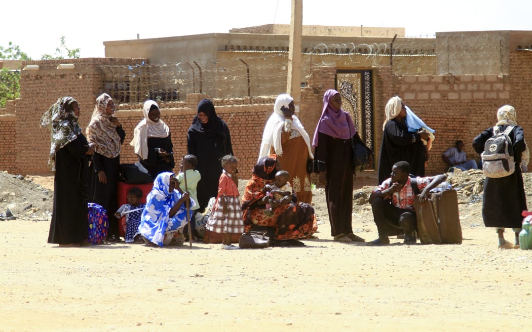 People fleeing street battles between the forces of two rival Sudanese generals, wait with their belongings along a road in the southern part of Khartoum, on April 21, 2023. - Hundreds of people have been killed and thousands wounded since the fighting erupted on April 15 between forces loyal to Sudan's army chief and the commander of the powerful paramilitary Rapid Support Forces (RSF). (Photo by AFP)