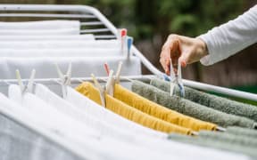 cropped shot of female hand hang fresh terry towels and fabric apparel on metal drying rack and using plastic clothespin in yard after laundry, housework duties
