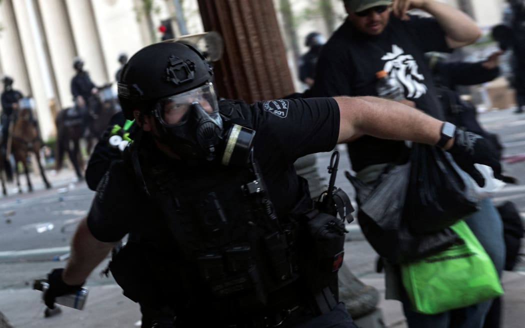 A Los Angeles police officer throws a tear gas canister at demonstrators as clashes erupt next to City Hall during a protest following federal immigration operations, in Los Angeles, California on June 8, 2025. Demonstrators torched cars and scuffled with security forces in Los Angeles on June 8, as police kept protestors away from the National Guard troops President Donald Trump sent to the streets of the second biggest US city. (Photo by ETIENNE LAURENT / AFP)