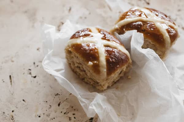 Two hot cross buns on a wrapper on a kitchen bench.