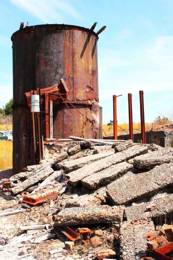 A rusty orange condensing tower at New Zealand's most toxic site, the historic Prohibition gold mine at Waiuta on the West Coast.  Surround but rusty metal and large lumps of broken concrete