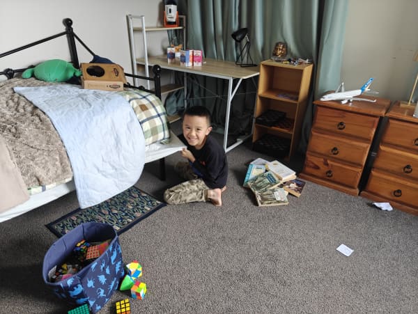 Raymond playing around at home in a room with a bag full of Rubik's cubes, books on the floor and board games in a shelf.