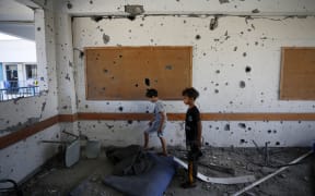 Young boys stand in a shrapnel-pocked room inside a UN-run school in the refugee camp of Al-Maghazi in the central Gaza Strip, a day after at least 6 people were killed in a reported Israeli strike, on October 18, 2023. Dozens of people, including UNRWA staff, were wounded and the school suffered severe structural damage, the United Nations agency for Palestinian refugees said. (Photo by Mohammed Faiq / AFP)