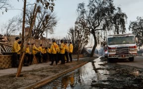 Firefighters take a short rest near houses burned down in the Palisades Fire along the Pacific Coast Highway in Malibu, California, January 9, 2025. 
Massive wildfires that engulfed whole neighborhoods and displaced thousands in Los Angeles remained totally uncontained January 9, 2025, authorities said, as US National Guard soldiers readied to hit the streets to help quell disorder. (Photo by David Pashaee / Middle East Images / Middle East Images via AFP)