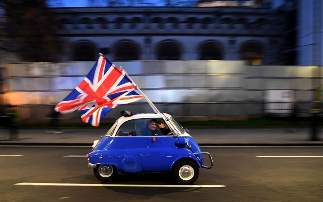 A man waves Union flags from a BMW Isetta as he drives past Brexit supporters gathering in Parliament Square, in central London on January 31, 2020, the day that the UK formally leaves the European Union