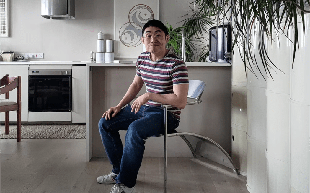 Cliff sits casually in a chair in his kitchen and smiles at the camera.