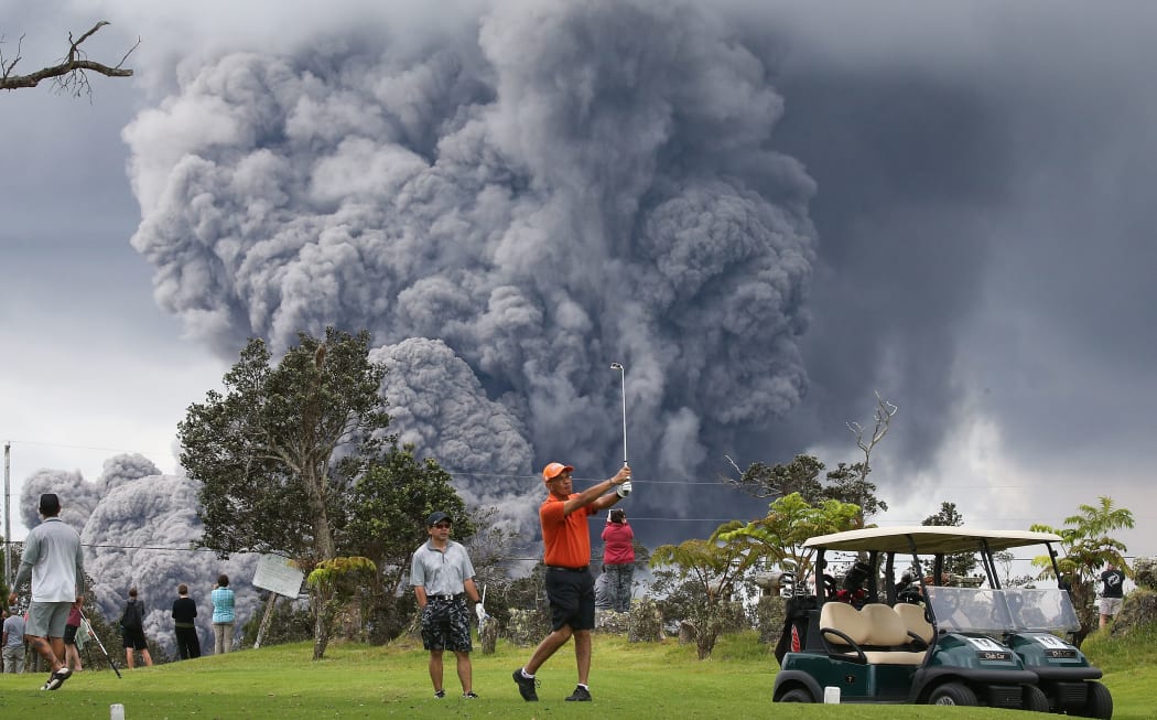 People play golf as an ash plume rises in the distance from the Kilauea volcano on Hawaii's Big Island.