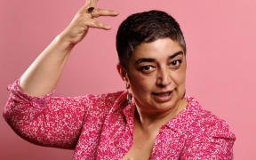 A photo of award winning storyteller, comedian, writer, director and political satirist Sameena Zehra. Sameena is holding her hands out in a gesture to the viewer.