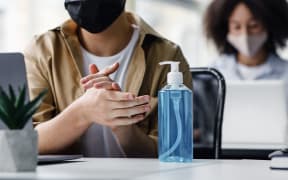 Focus on antiseptic to protect against covid virus. Guy disinfects his hands, sitting at table at workplace with laptop, working in interior of modern office, panorama, copy space