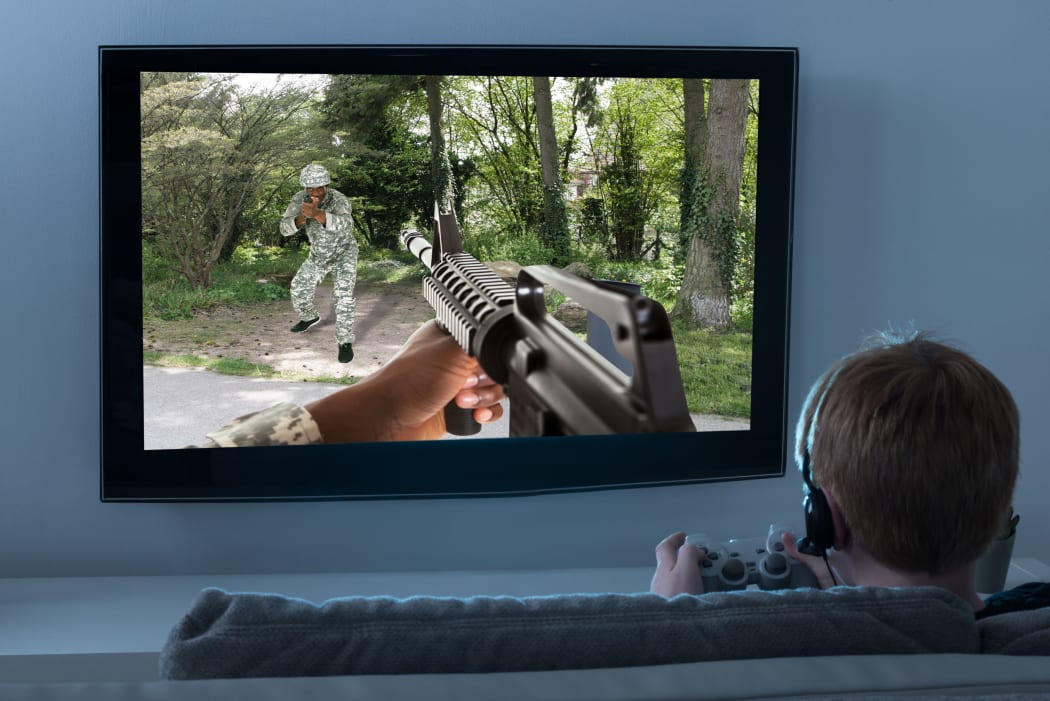 A photo of a Boy Sitting On the Sofa Playing an Action Game involving guns On Television