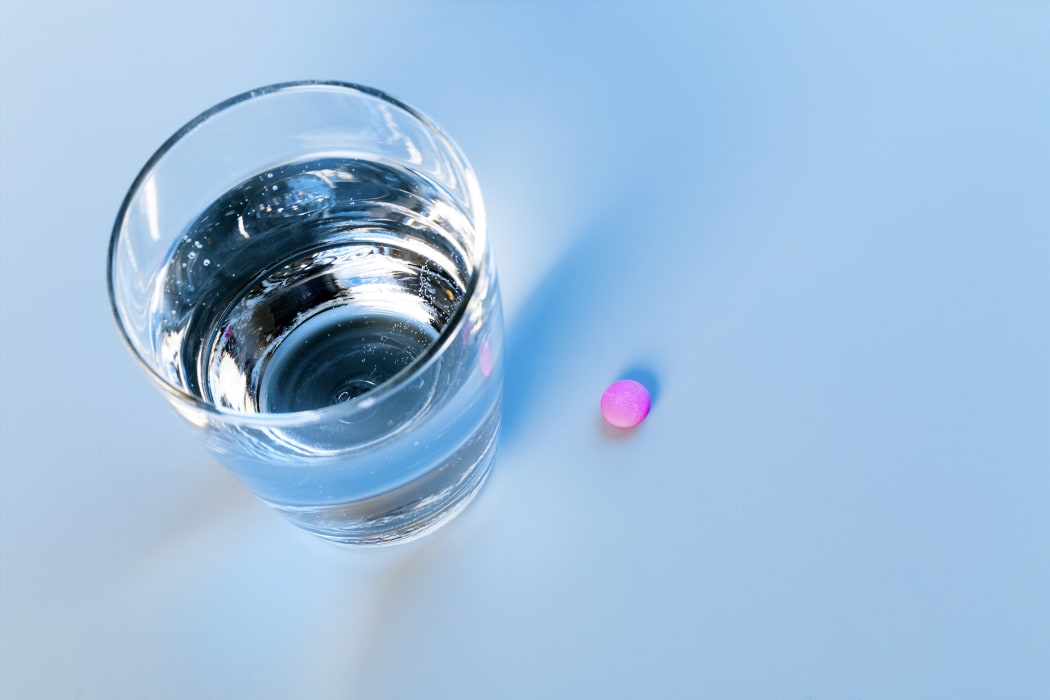 A pink pill next to a glass of water (stock photo)