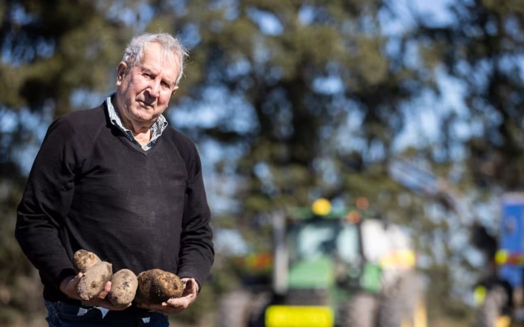 Allan Pye, the "Spud King" holding potatoes with a tractor in the background.