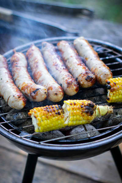 A barbecue plate with corn cobs and sausages being cooked.