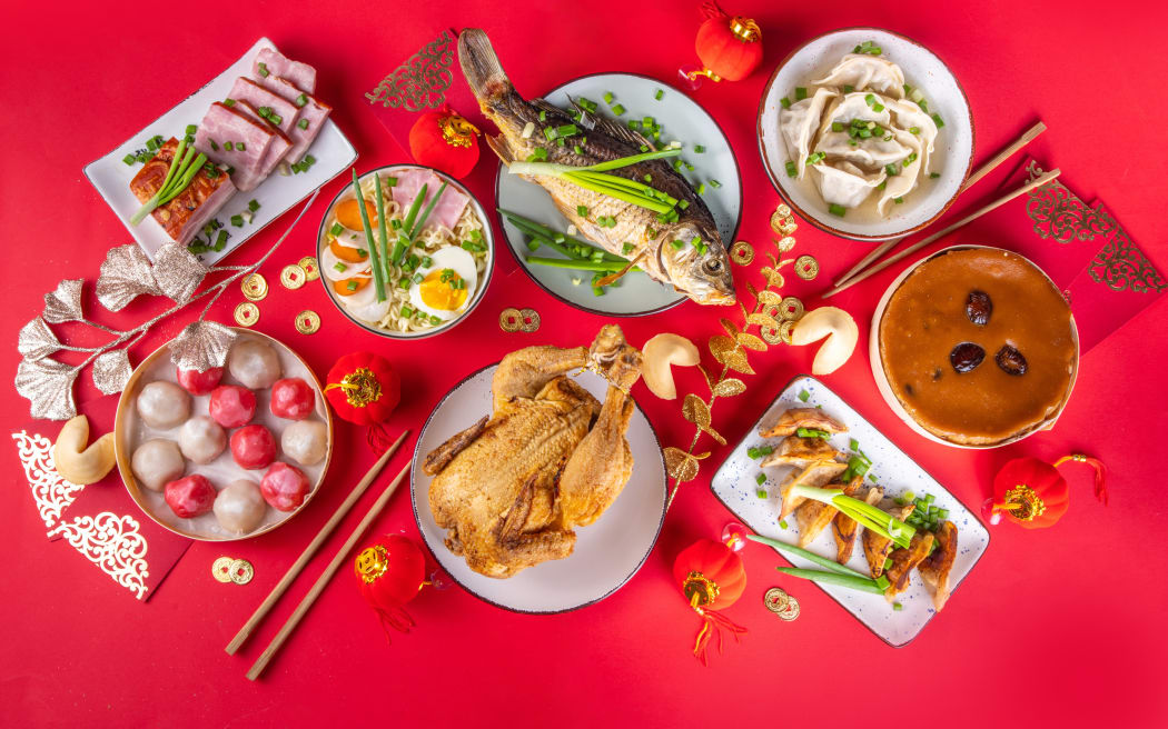 Traditional Chinese lunar New Year dinner table, party invitation, menu background with pork, fried fish, chicken, rice balls, dumplings, fortune cookie, nian gao cake, noodles, chinese decorations