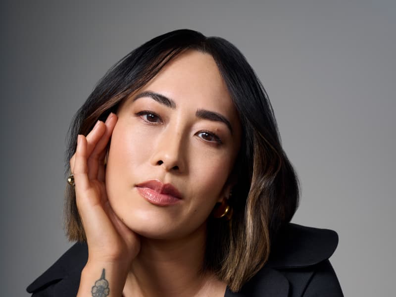 Mellissa Leong, a 43 year old Asian woman with a shoulder length bob, cups her face with one hand and stares at the camera.