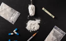 Cocaine and other drugs on a black background, close-up. A rolled up dollar bill for drug use. Prohibited drugs.