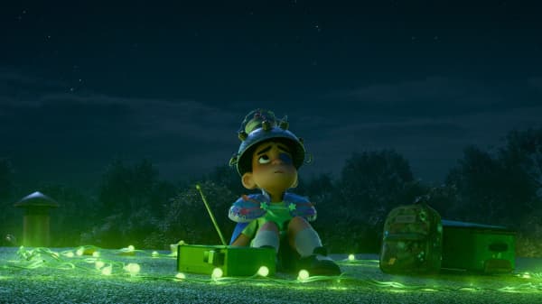 Elio, a young boy in an animation movie, looks up at the sky with a metal helmet on his head and string of lights on the ground.