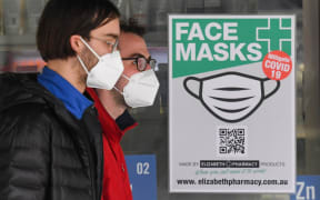People wearing face masks walk past a sign advertising masks in Melbourne on July 20, 2020.