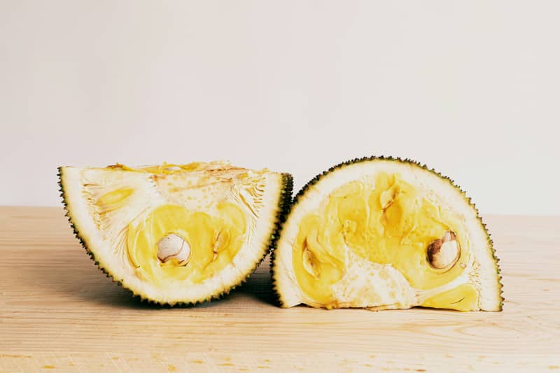 A jackfruit sliced open in half on a wooden table.