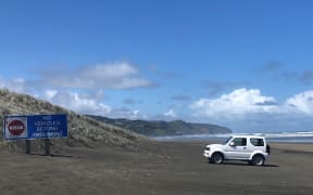 A white four-wheel driving is parked near a sign saying 'no vehicles beyond this point' on Muriwai Beach