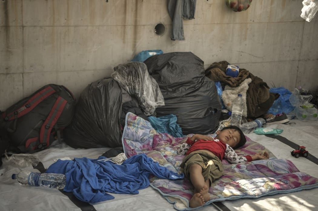 A child sleeps along the roadside where thousands are living with out shelter and exposed to the elements following the burning down of their camp.