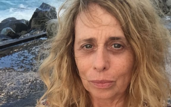 Film director Janine Hosking stands on a rocky beach.