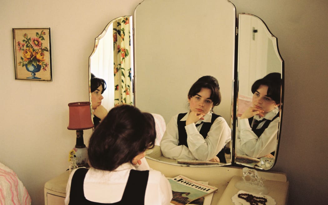 Mary (Maya Le Roux) looks at her reflection in the mirror in her bedroom.
