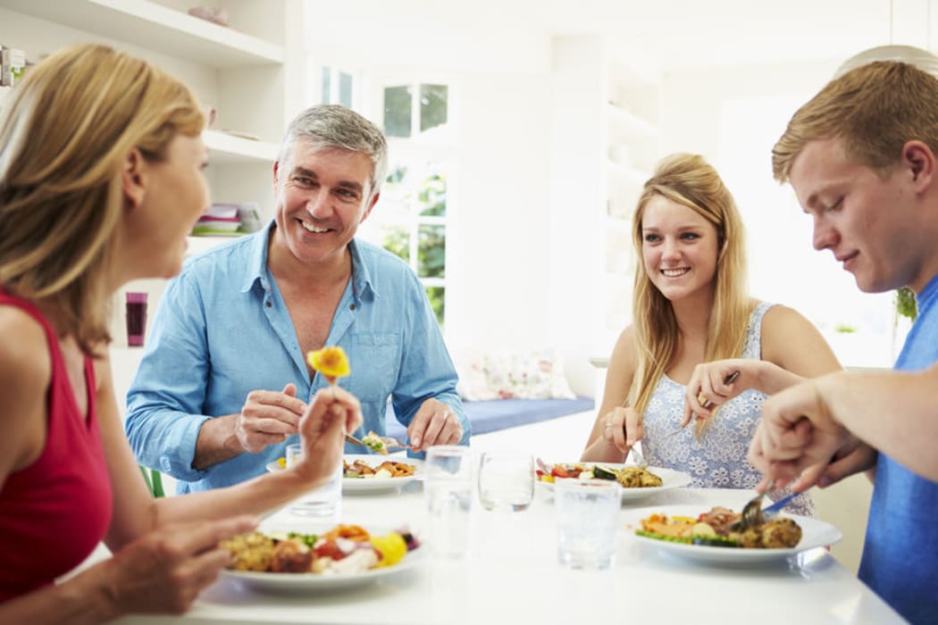 A photo of a family with teenage children eating meal at home together