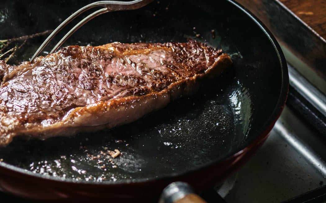 A person cooking a steak in heavily oiled pan with fats coming out.