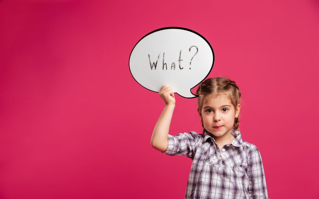 Image of pretty little girl child standing isolated over pink background. Looking camera holding speech bubble.