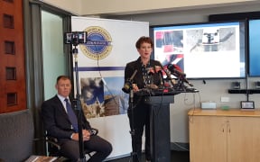 TAIC's chief commissioner Jane Meares and chief investigator Tim Burfoot speak at the presser with the pair of over-trousers pictured in the background.
