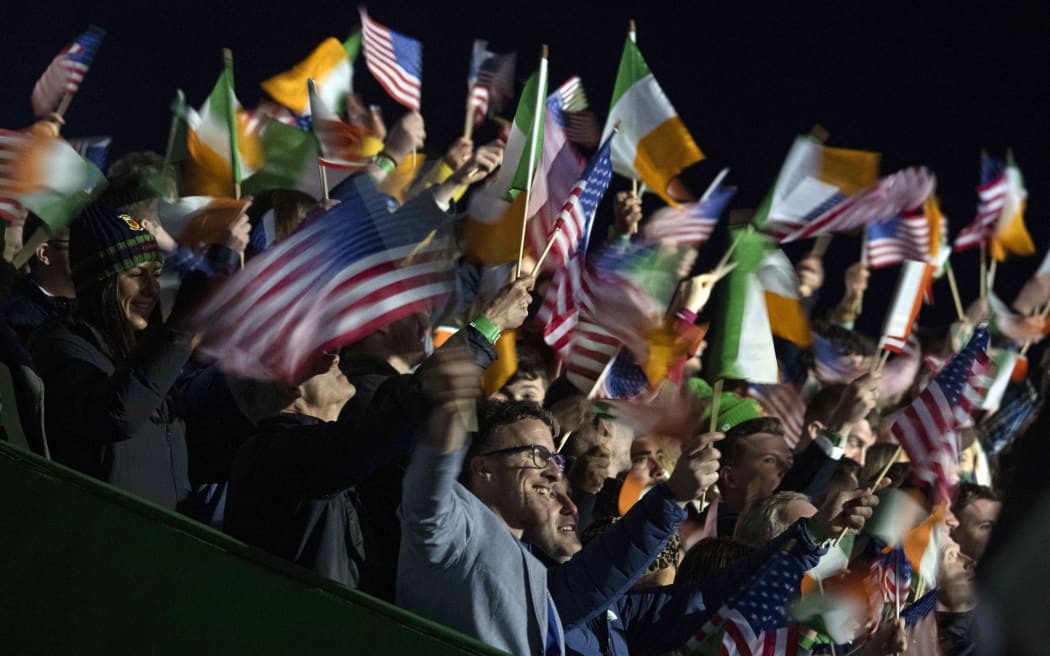 Audience members wave flags while waiting for US President Joe Biden to arrive to deliver a speech at Saint Muredach's Cathedral in Ballina, on April 14, 2023, on the last day of a four day trip to Northern Ireland and Ireland.