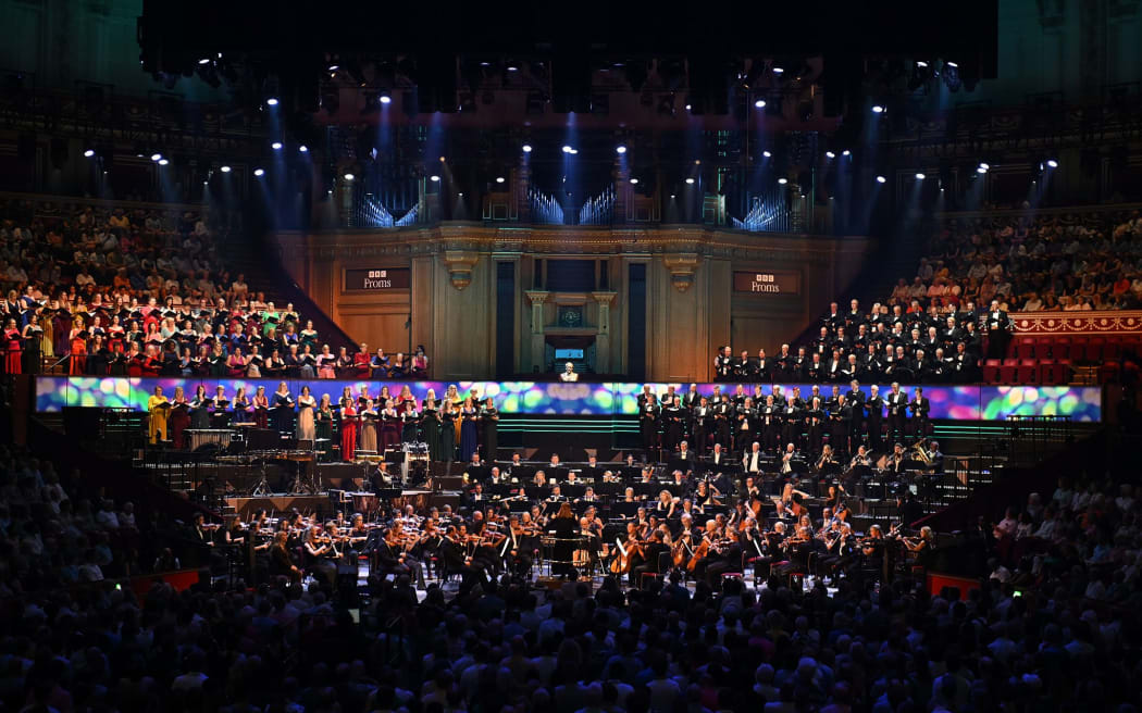 Orchestra, choir, audience in a concert hall under colourful lighting.