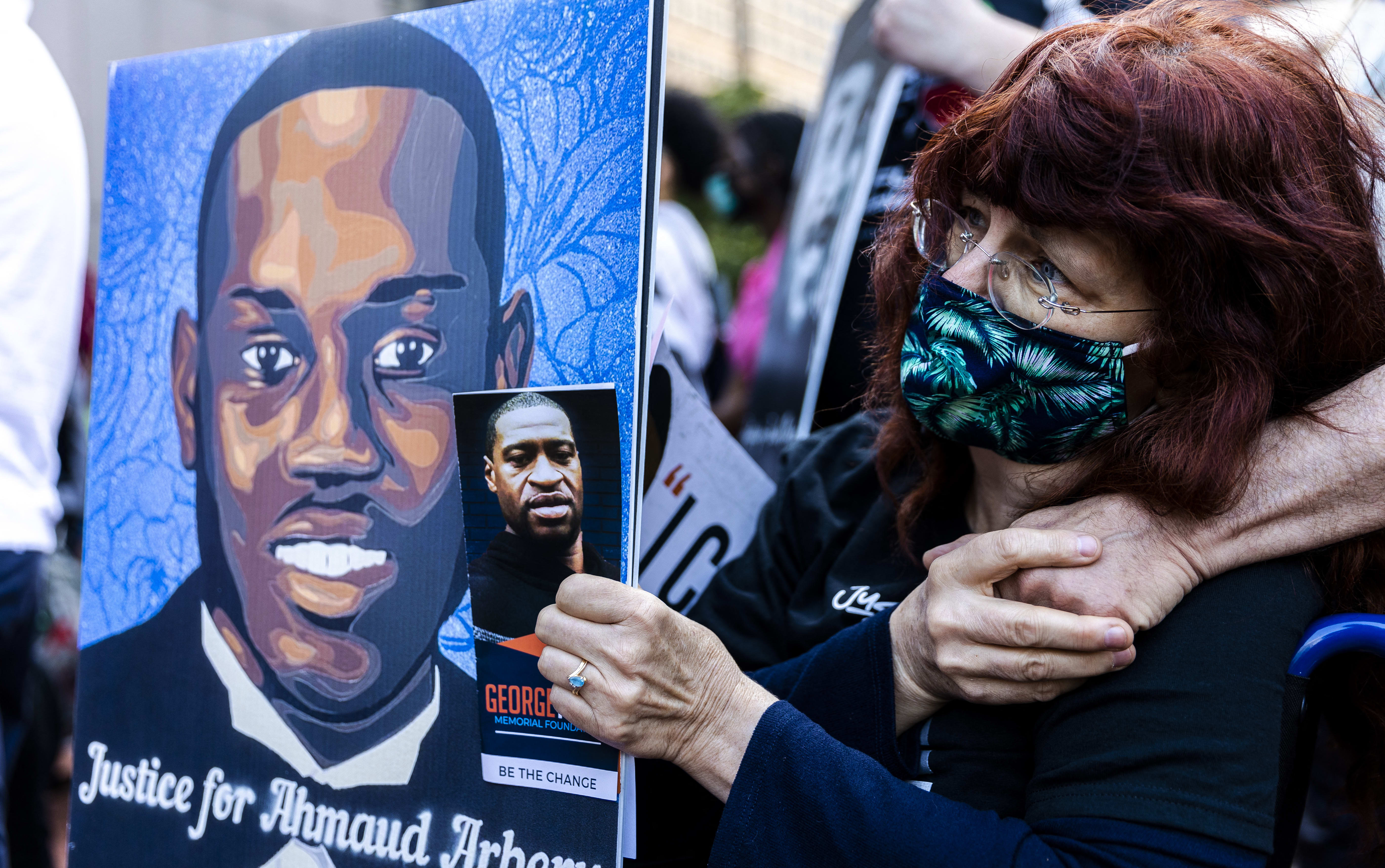 Racial justice demonstrations were held around the US after word of Ahmaud Arbery's death spread. A woman holds a portrait of Arbery, and George Floyd at a remembrance event in May 2021 in Minneapolis..