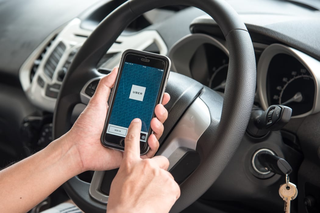 A man hand holding screenshot of Uber app in a car.