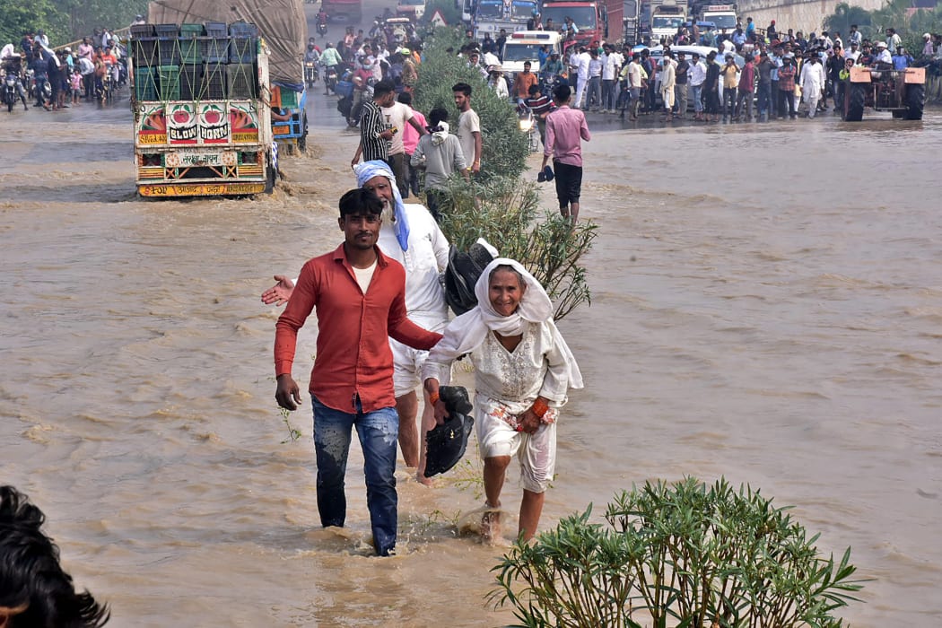 Commuters wade through a flooded national highway after river Kosi overflowed following heavy rains near Rampur in India's Uttar Pradesh state on October 20, 2021.