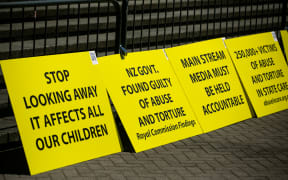 Signs from protestors sit outside Parliament during the apology for abuse in state care