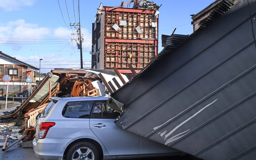 A car is seen under part of a roof in Anamizu, Ishikawa Prefecture on 4 January, 2024, after a major 7.5 magnitude earthquake struck Japan's Noto region on New Year's Day.