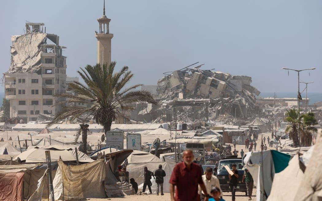 Palestinians walk past tents for displaced people set up near the debris of Mushtaha Tower in Gaza City following an Israeli military strike on September 5, 2025, amid the war between Israel and the Hamas militant movement. The Israeli military said it struck a high-rise in Gaza City on September 5, shortly after announcing it would target tall buildings identified as being used by Hamas ahead of its forces' planned conquest of the urban hub. (Photo by Omar AL-QATTAA / AFP)