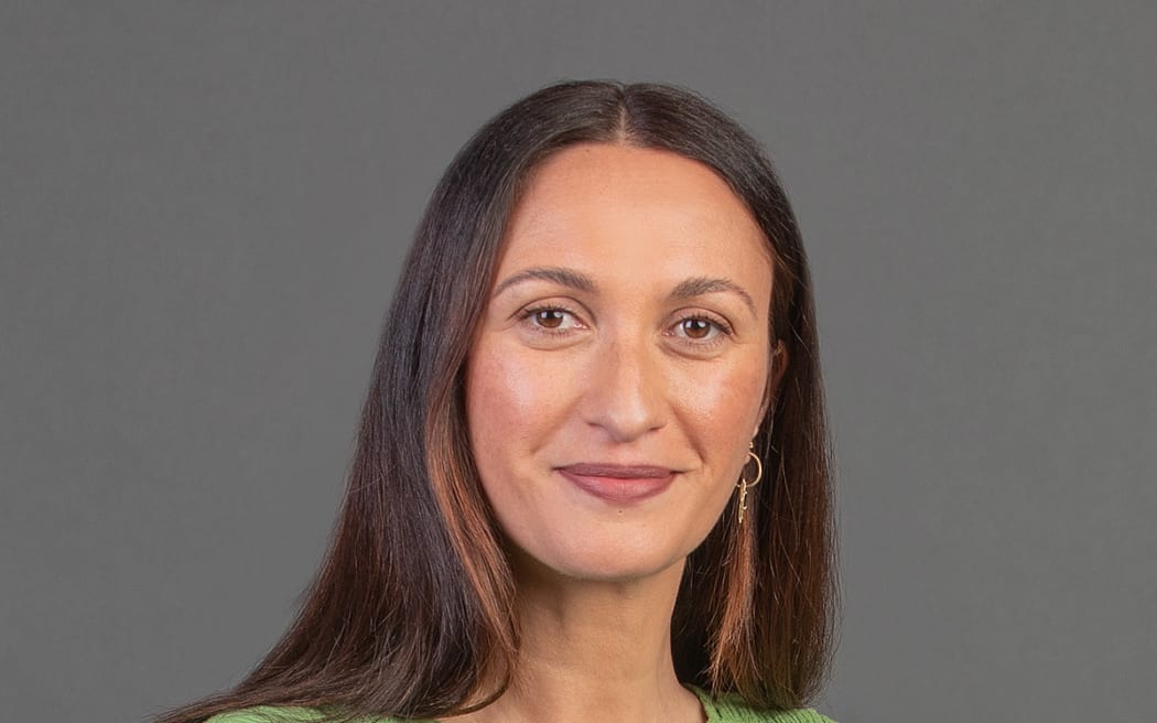 Kara Rikard stands in a studio on a grey backdrop in a green top