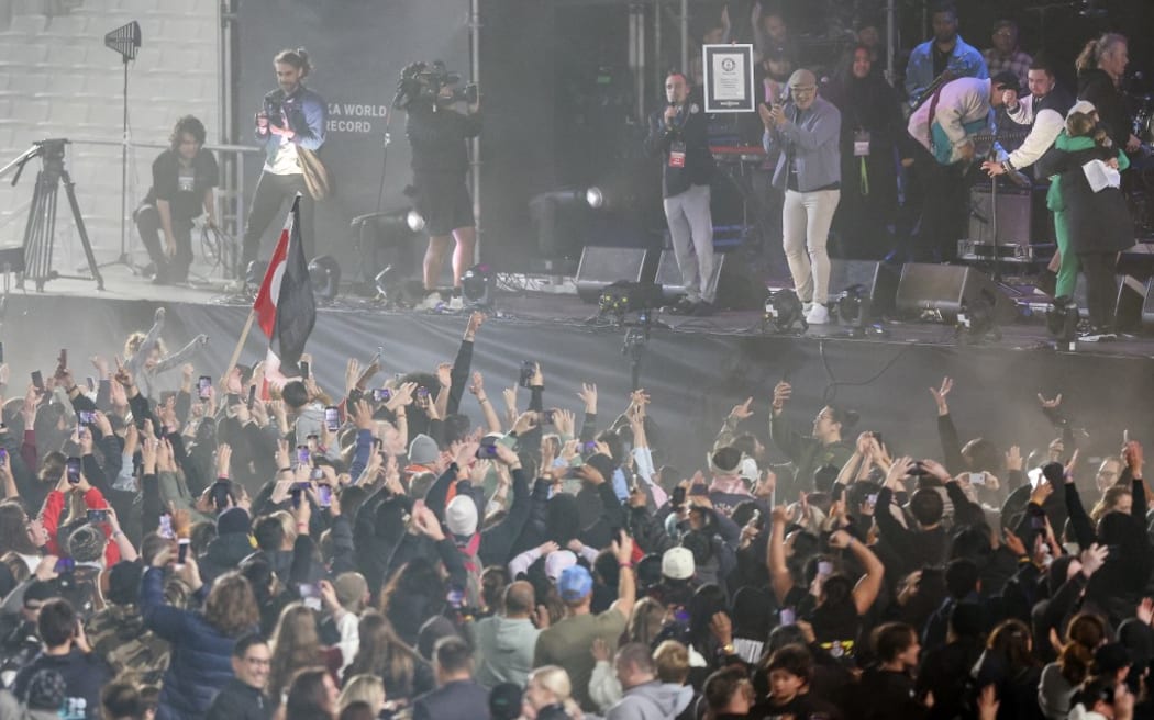 Guinness World Records adjudicator Brian Sobel (center L, onstage) holds up a plaque as he officially announces a new record for the largest mass Haka, at Eden Park in Auckland on September 29, 2024. The gathering on September 29 smashed the previous record, officially held by France since 2014, of the Maori war dance made famous by the All Blacks. (Photo by DJ Mills / AFP)