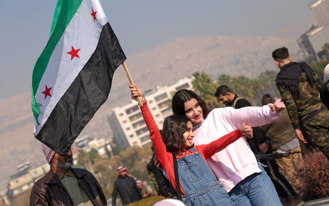Two girls pose for photos while waving a Syrian opposition flag at Umayyad Square in Damascus.