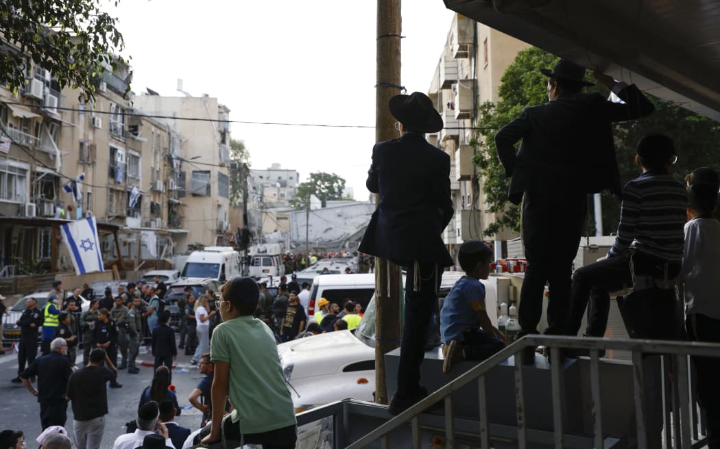 People watch as rescuers work near a damaged building following a strike by an Iranian missile in the Israeli city of Bnei Brak.