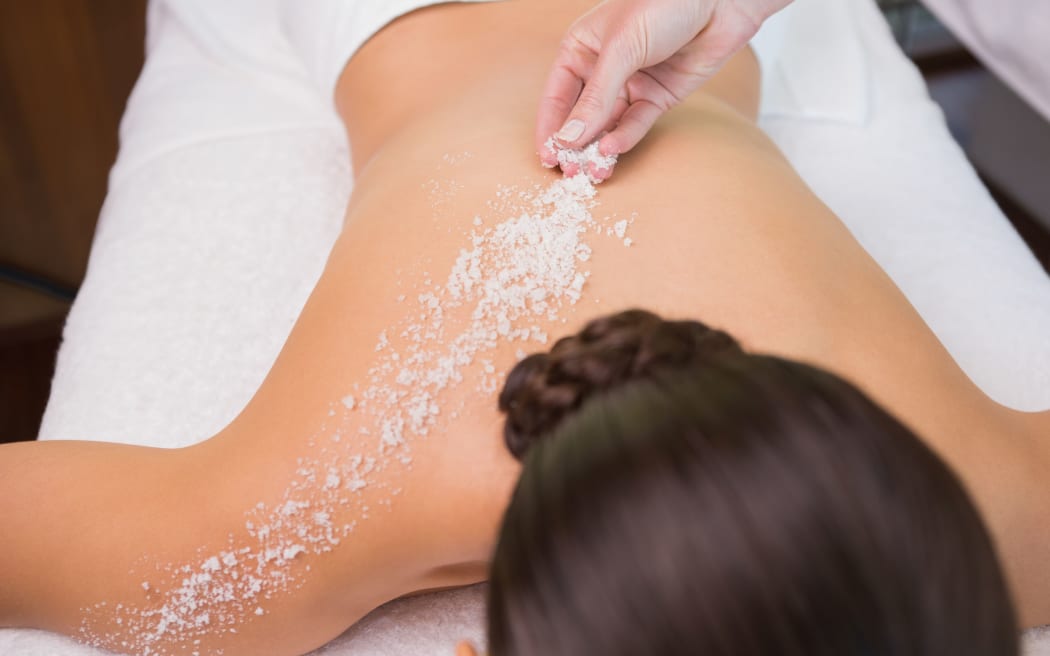 Beauty therapist pouring salt scrub on womans back in the health spa