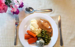 A home cooked meal sits on a china plate on a gingham tablecloth